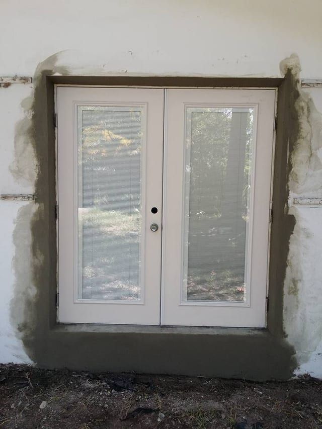Same french doors stuccoed in with a clean scratch-coat patch around the frame