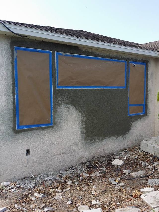 Same wall with windows masked off and a fresh wet scratch coat over the block