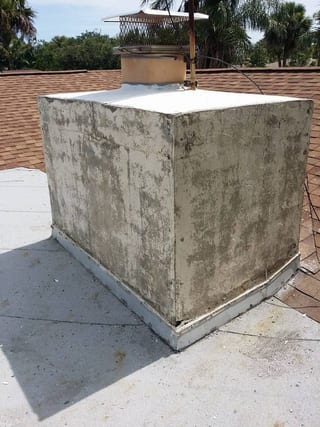 Weathered chimney with damaged stucco at the roof line before repair